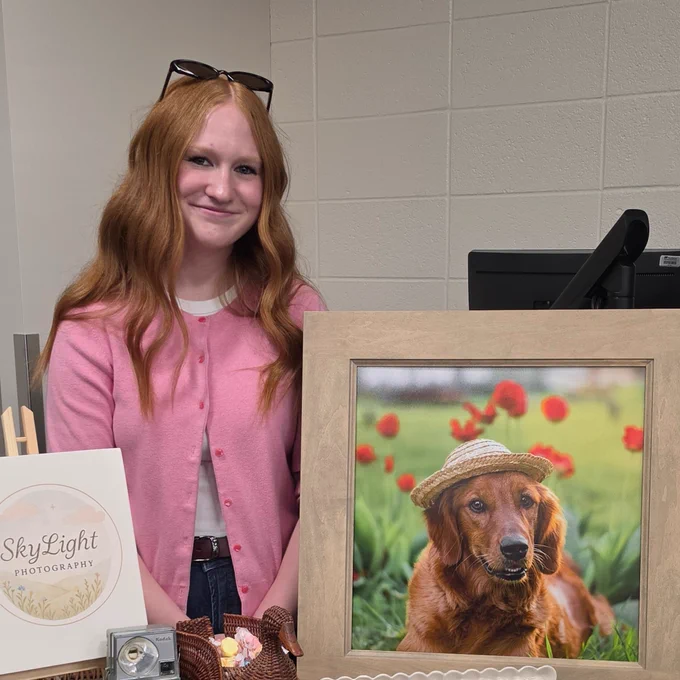 A person stands behind a display table featuring framed photos of a golden retriever.