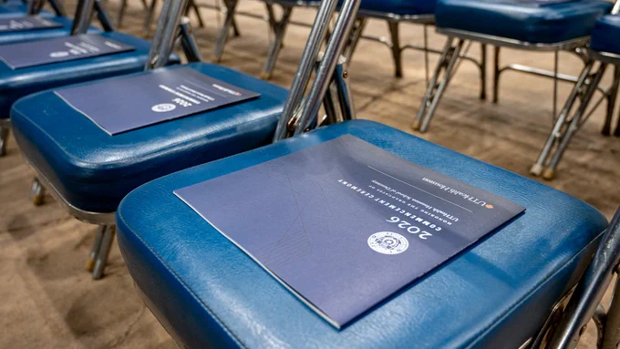 Rows of blue padded folding chairs are arranged for a ceremony, each seat holding a dark‑blue booklet labeled “2026 Commencement Ceremony” with the UTHealth Houston seal and branding.