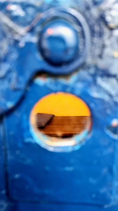 a peep hole in a blue cell door - a wooden bench can be seen in the cell within