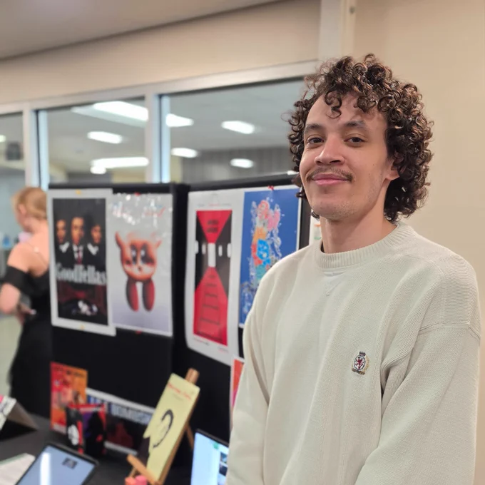 A person with curly hair stands beside a display table.