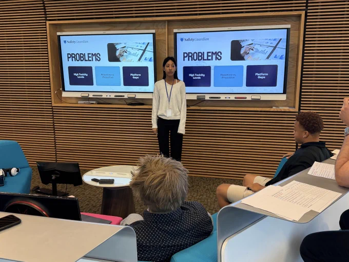 A woman standing in front of a classroom, giving a presentation with problems and solutions displayed on the screens behind her.