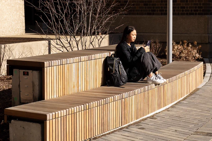 A woman sitting on a bench outside looking at her phone
