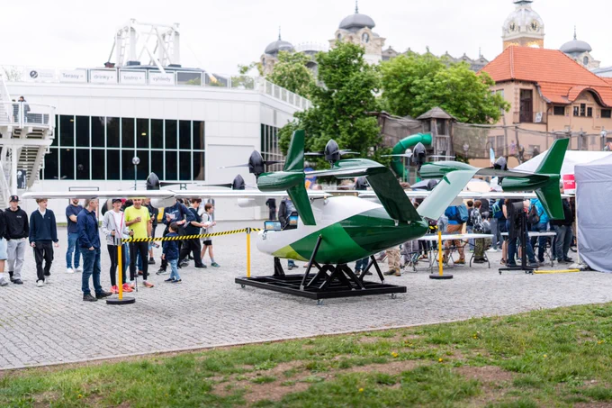 Zuri's TD 2.0 display aircraft at Výstaviště Praha, visitors gathered around, Industrial Palace clock tower behind.