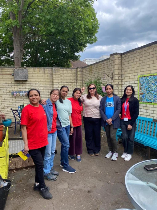 Group from Lexis Nexis and Amanda standing outdoors in a courtyard with brick walls, colourful benches, and hanging plants under a cloudy sky.