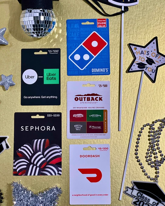Various gift cards including Uber Eats, Domino's, Outback Steakhouse, Sephora, and DoorDash arranged on a table with graduation-themed decorations.