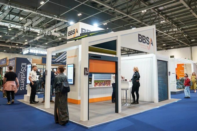 A bustling trade show exhibit featuring a modern booth for BBSA and ID Systems. Attendees engage with interactive displays and representatives amidst a backdrop of innovative products.