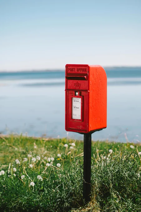 Photo by Jilly Noble of red postbox next to seaside. https://www.pexels.com/photo/iconic-red-post-box-by-avoch-seaside-32129130/