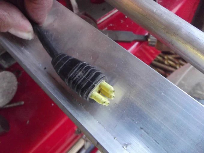 An electrical connector with four yellow pins arranged in a trapezoidal fashion on the end of a black wire.