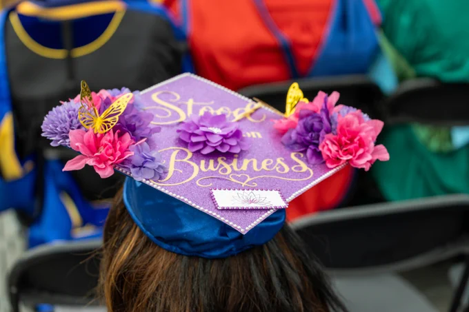 Graduation cap decorated with pink and purple flowers, yellow butterflies, and the words "Stood on business.