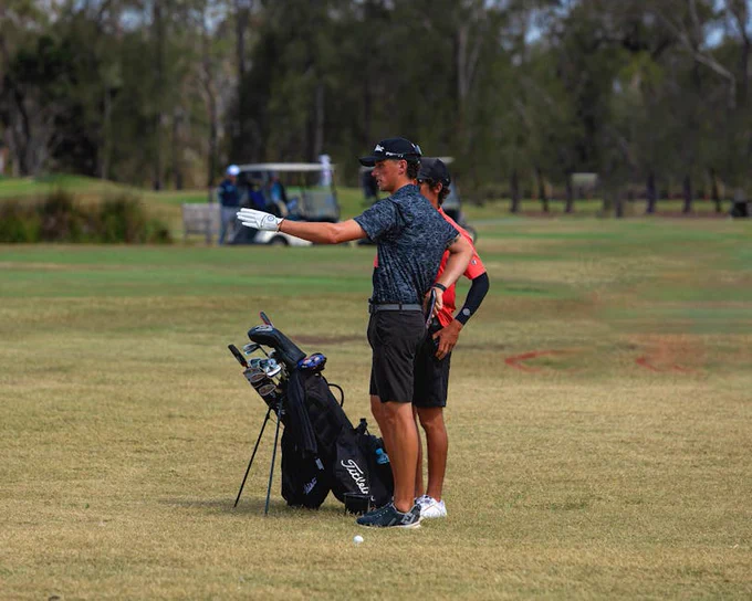 Two golfers discussing strategy on a sunny golf course with equipment nearby.
