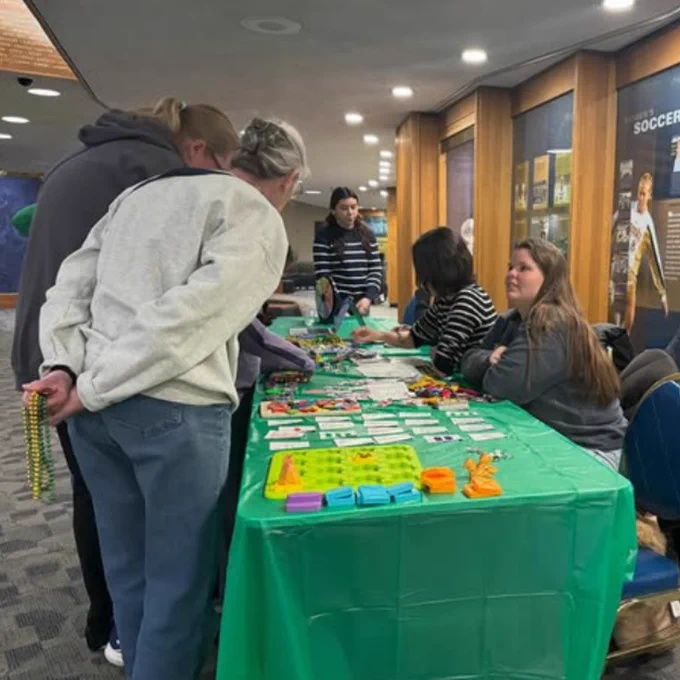 Representatives from the Notre Dame AWM Student Chapter sitting at an event table with colorful math items and talking with visitors.