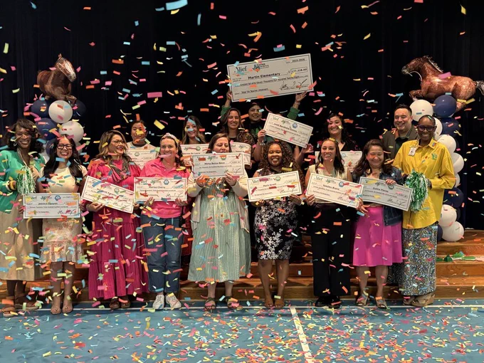 People stand on a stage holding certificates and smiling, with confetti falling and balloons behind.