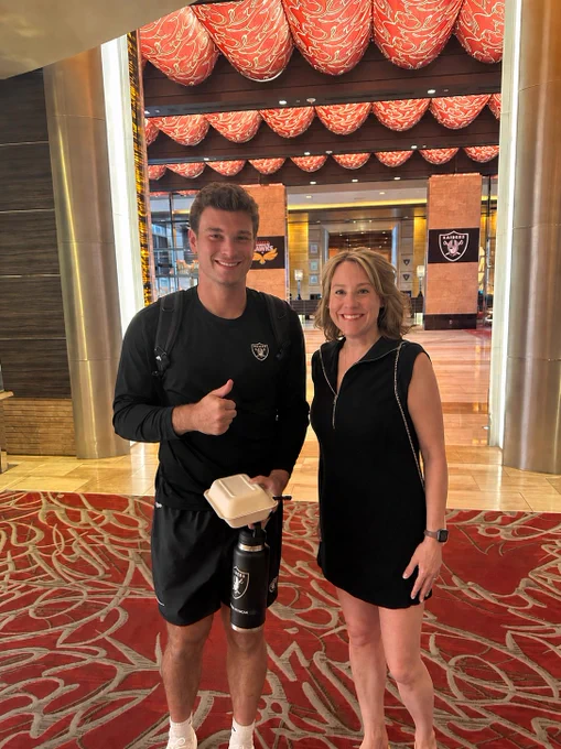 Michelle Malaska and Fernando Mendoza standing together in a Vegas hotel lobby. Mendoza is holding a take-out box and giving a thumbs up.