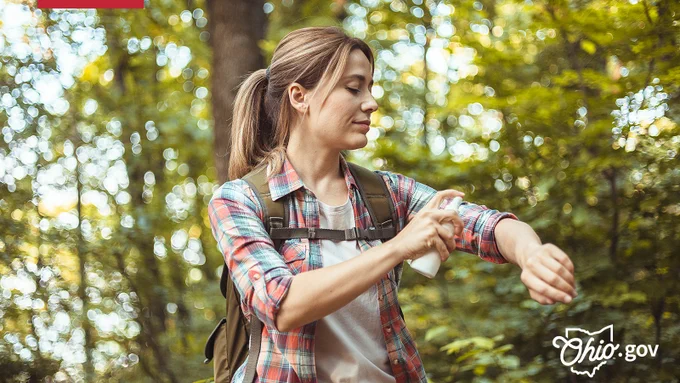 A woman sprays mosquito repellent on her arms while hiking.