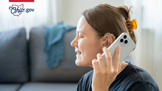 A woman with hearing aids holds a smartphone up to her ear.