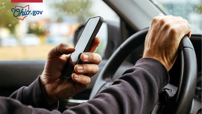 A man holds a smartphone while he sits behind the steering wheel of a car.