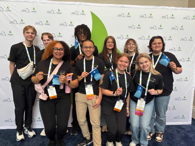 10 students from Elk River and Sauk Rapids-Rice high schools stand together at the ProStart competition holding their Minnesota flags
