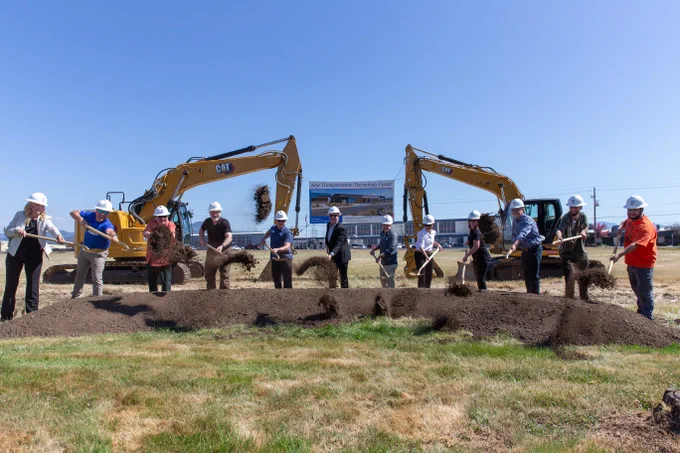 A group of people from RCC and the local community participate in a groundbreaking ceremony, shoveling dirt in front of two large Caterpillar excavators. A banner in the background displays text, indicating a new construction project. This is at Table Rock Campus.