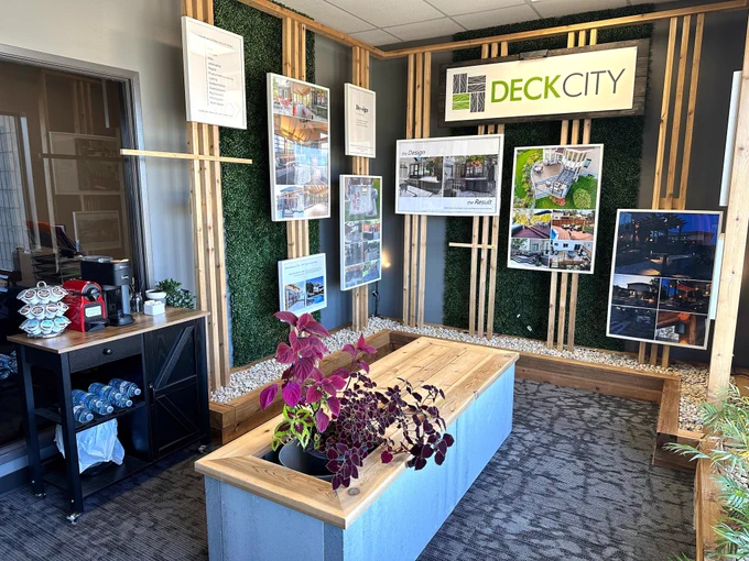 Deck City showroom interior featuring design displays, project photos, wood accents, greenery walls, and a seating area with a coffee station nearby.