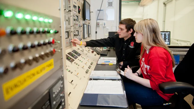 Two people work at the control panel for the nuclear reactor.