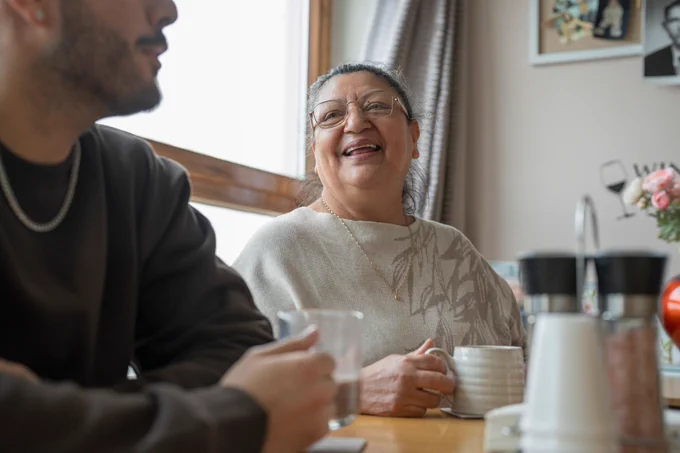 A picture showing a woman and a man sat at a table having a chat and drinking coffee.
