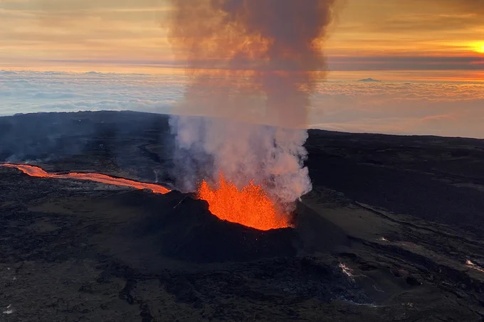 Glowing lava erupting from a volcanic crater with thick smoke rising against an early morning sky.