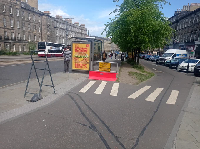 Elm Row Bus stop viewed from the south, with a new barrier and sign blocking the cycle lane next to the bus stops. An empty road sign frame is on the pavement.
