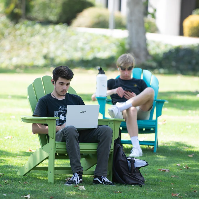 two adirondack chairs on campus with a student in each.