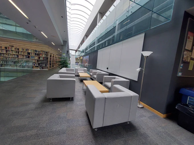 Comfy chairs and sofas arranged in a rectangle with a whiteboard on the wall, a large skylight above and a plant and book shelves in the background