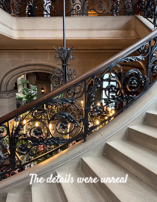 Elegant staircase inside the Biltmore Estate with curved stone steps and intricate black iron railings illuminated by warm lights below.