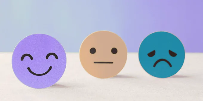 Three round emoji faces on a flat surface against a gradient background. From left to right: a purple happy face, a beige neutral face, and a teal sad face.