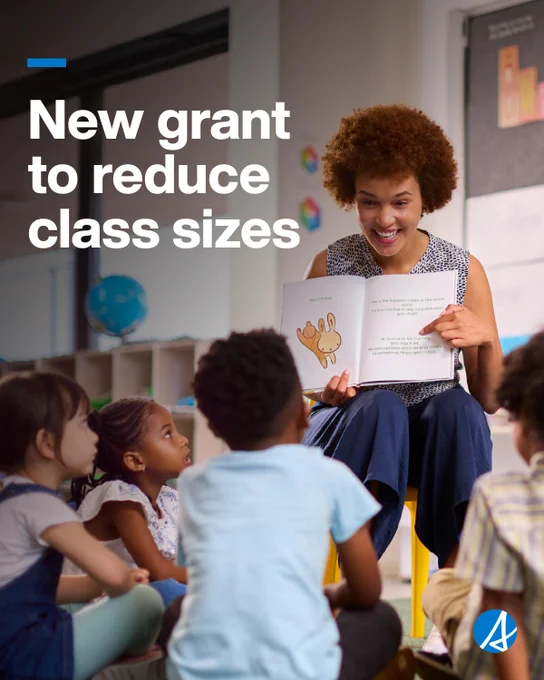 A teacher sits in a classroom reading a picture book aloud to a small group of young children gathered around her. Large white text on the left side of the image reads, “New grant to reduce class sizes.” A blue logo appears in the bottom-right corner.