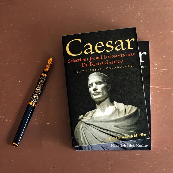 Image is a photo of two books for teaching high school and college Latin translation. The books are titled, "Caesar: Selections from His Commentarii De Bello Gallico." There is a student textbook and a teacher guide. An elegant fountain pen is on the desk beside the books, ready to take notes in Latin.