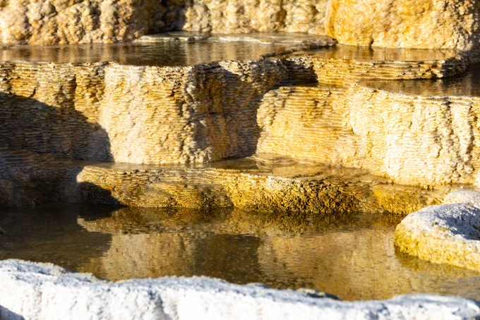 A close-up of layers of colorful rocky terraces, with colors ranging from stark white, yellow, to orange. Small hot spring pools are seen on the layers. These terraces are a part of a larger hydrothermal feature called Palette Spring.