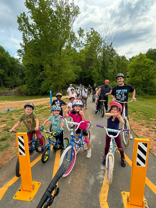 Family-friendly bike ride with children and adults on a sunny day along a tree-lined path.
