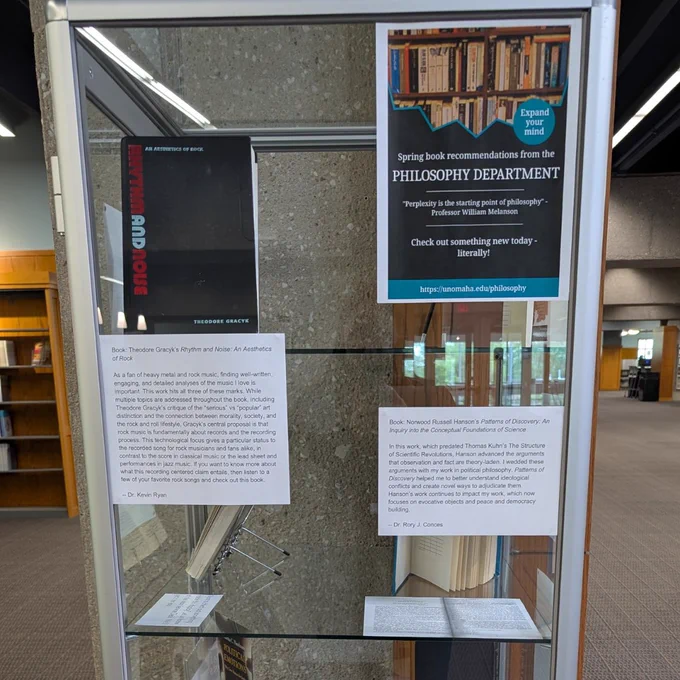 A glass and metal library display case with books in the case. There are explanations visible on the front of the case.