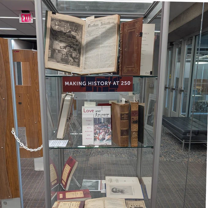 A glass and metal library display case with books in the case. 