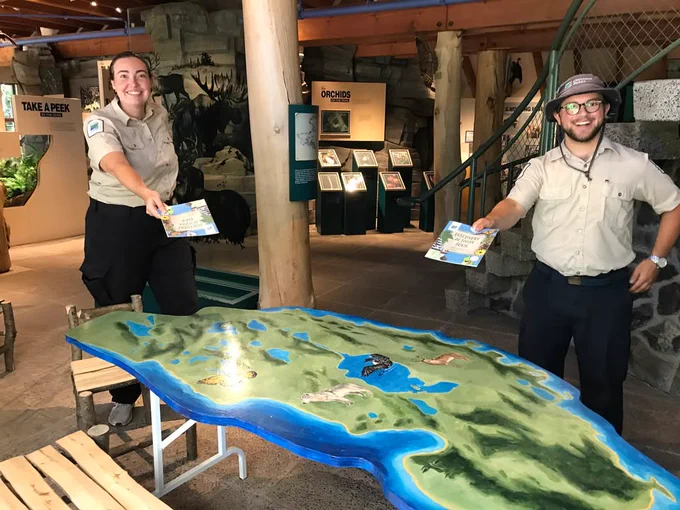 Two people in uniform stand next to a large topographical model of a landscape inside a visitor center. 