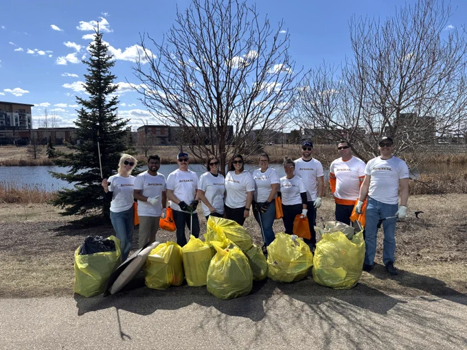 Group of volunteers standing outdoors with collected trash bags after a cleanup event near a pond and trees. 