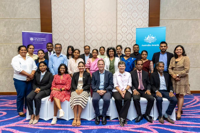 Group photo of participants and course staff posing indoors with banners from The University of Queensland and Australia Awards behind them.