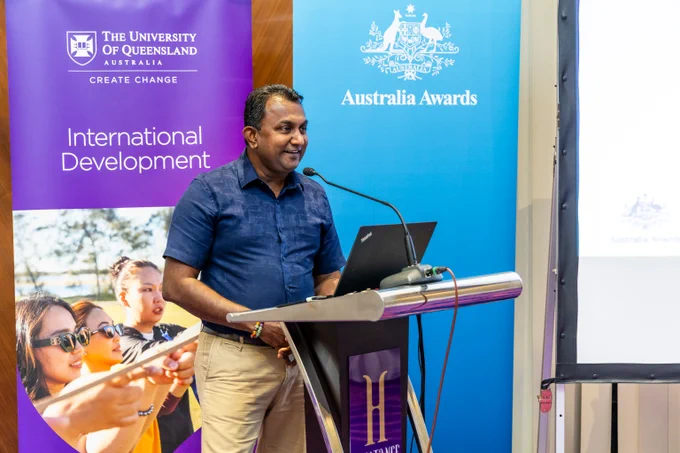 Man in blue shirt speaking at a podium during an event hosted by The University of Queensland and Australia Awards.