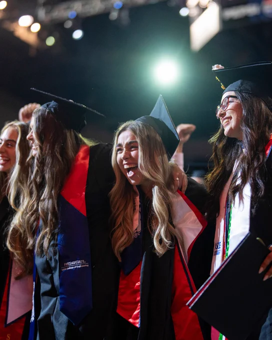 Student cheering in crown in graduation regalia.