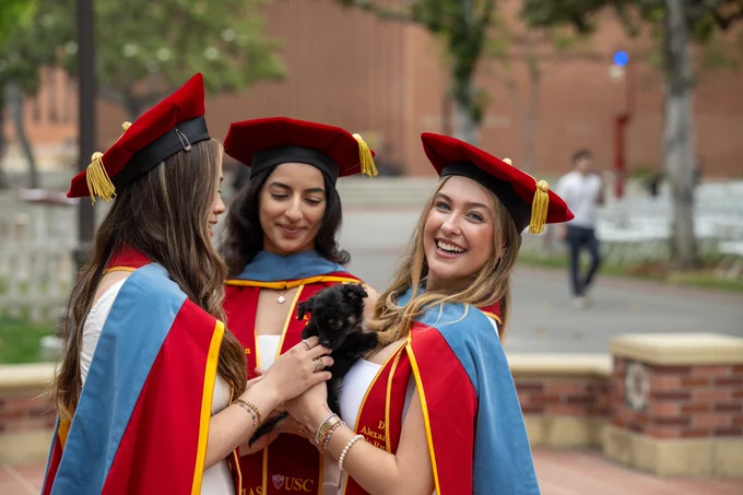 Students in Commencement regalia posing for a photo with a puppy