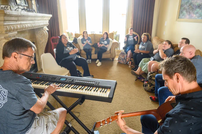 Michael holding guitar and David at keyboard, with group of attendees across the background.