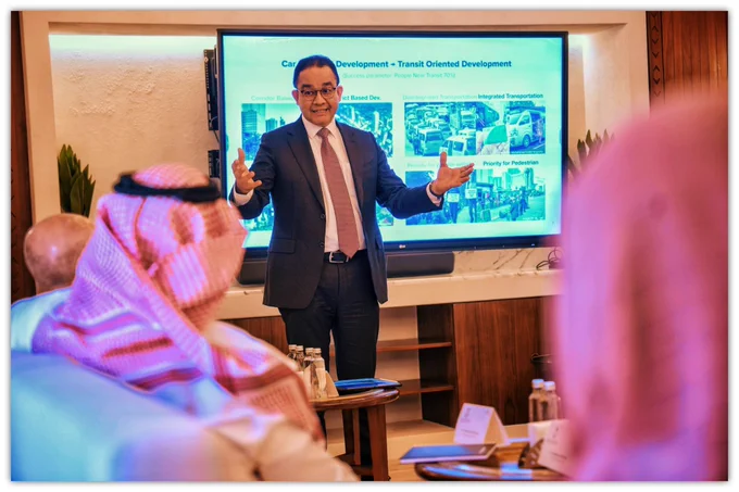 Anies Baswedan berdiri di depan layar presentasi saat berbicara dalam sebuah sesi diskusi di Riyadh Competitiveness Forum.

Mengenakan setelan jas gelap dan dasi merah muda, ia tampak menjelaskan konsep pengembangan kota dan transportasi berbasis transit kepada para peserta forum yang duduk menghadapnya, beberapa mengenakan pakaian tradisional Arab Saudi.

Di belakangnya terlihat slide presentasi bertema pengembangan perkotaan dan integrasi transportasi, mencerminkan perannya sebagai anggota dewan penasihat Komisi Kerajaan untuk Kota Riyadh.
