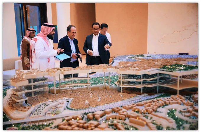 Anies Baswedan bersama anggota dewan penasihat Riyadh Competitiveness Forum dan perwakilan pengelola kawasan berdiri mengelilingi sebuah maket besar rencana pengembangan kawasan Ad Diriyah di pinggiran Kota Riyadh.

Dalam suasana diskusi yang hangat, Anies tampak menunjuk ke salah satu bagian maket sambil berdialog dengan peserta lain mengenai desain kawasan dan pengembangan kota.

Maket detail yang menampilkan tata ruang, bangunan, dan lanskap wilayah menjadi pusat perhatian, mencerminkan visi transformasi urban dan pelestarian kawasan bersejarah Ad Diriyah sebagai bagian dari pengembangan Riyadh modern.