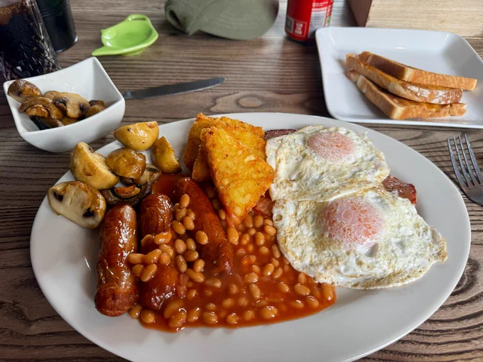 A fry up containing sausages, bacon, hash brown, eggs, mushrooms, beans and toast