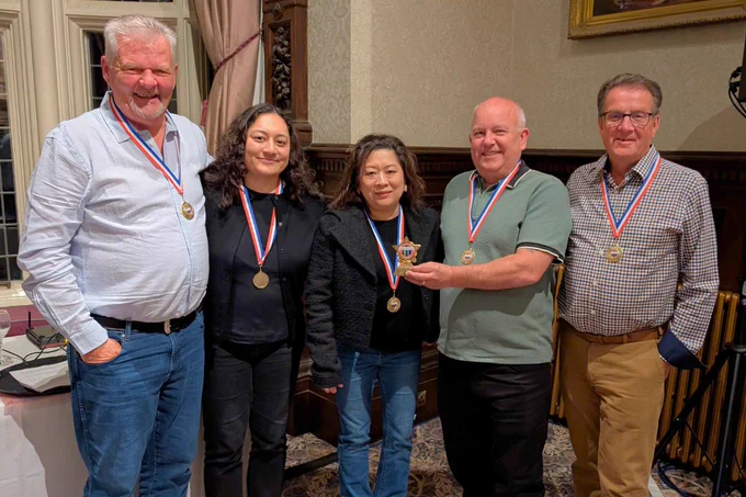 Five pub quiz winners standing in a row wearing medals around their necks, with one person holding a small trophy.