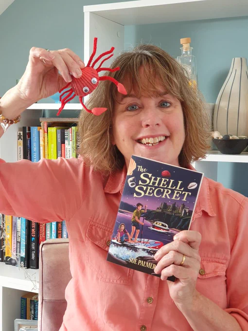Woman holding a shell crab craft and the book "The Shell Secret" by Sue Palmer.