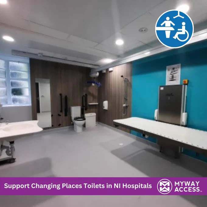 A modern Changing Places toilet facility with a height-adjustable changing bench, ceiling hoist, accessible toilet, grab rails and wash basin. A purple banner at the bottom reads “Support Changing Places Toilets in NI Hospitals” alongside the My Way Access logo. A Changing Places symbol appears in the top right corner.